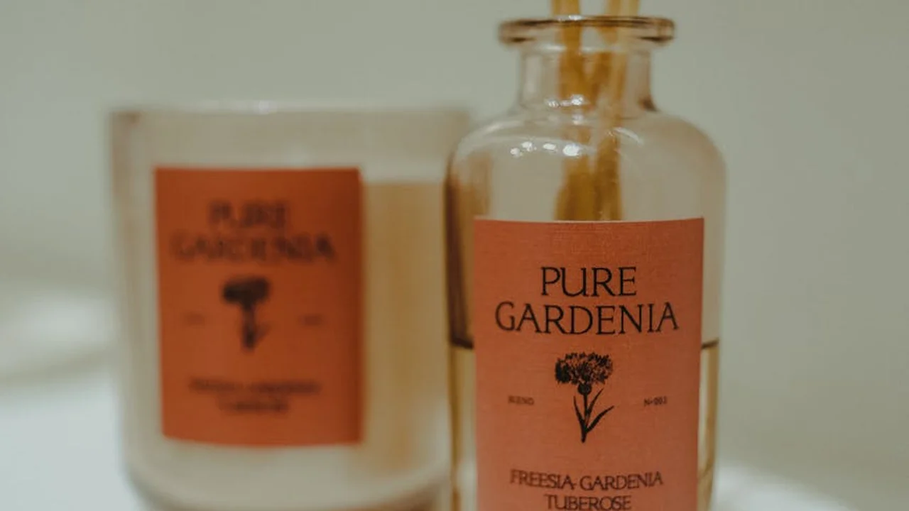 Close-up of a glass reed diffuser bottle labeled 'Pure Gardenia' on a countertop, with a blurred candle in the background.