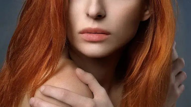 Close-up portrait of a woman with long red hair, touching her shoulder