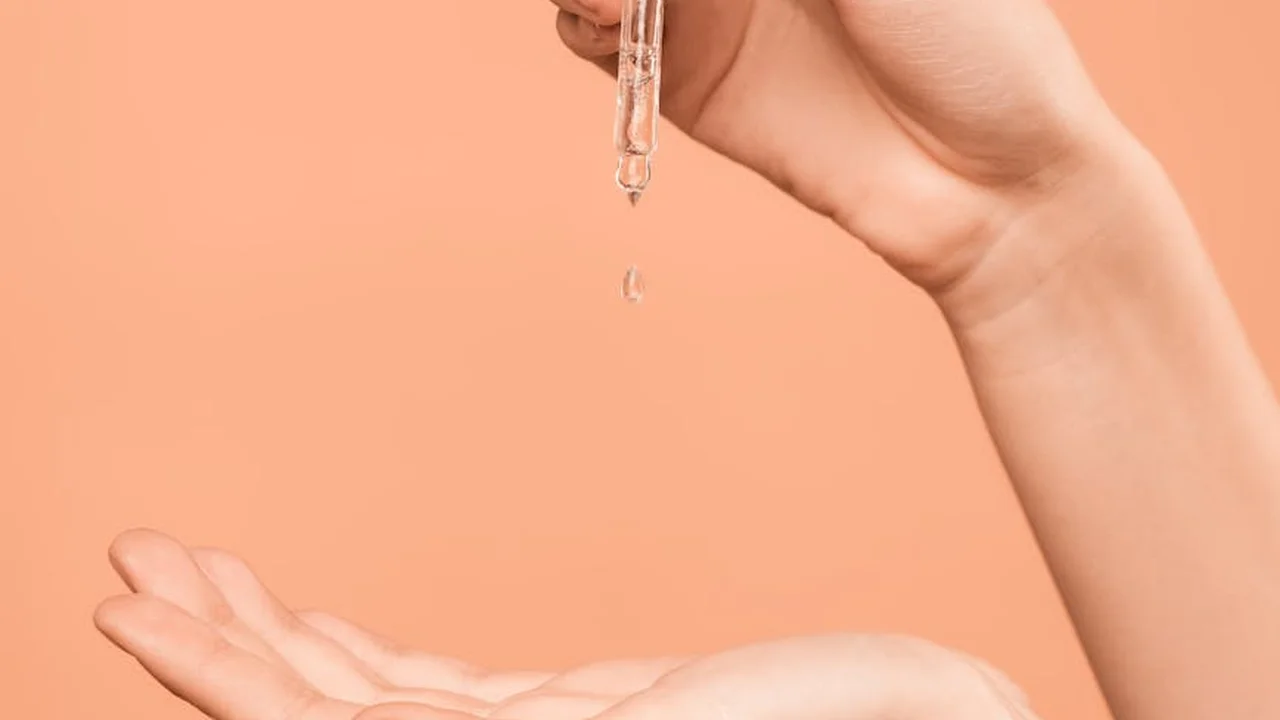 Dropper releasing oil onto a hand against a peach-colored background