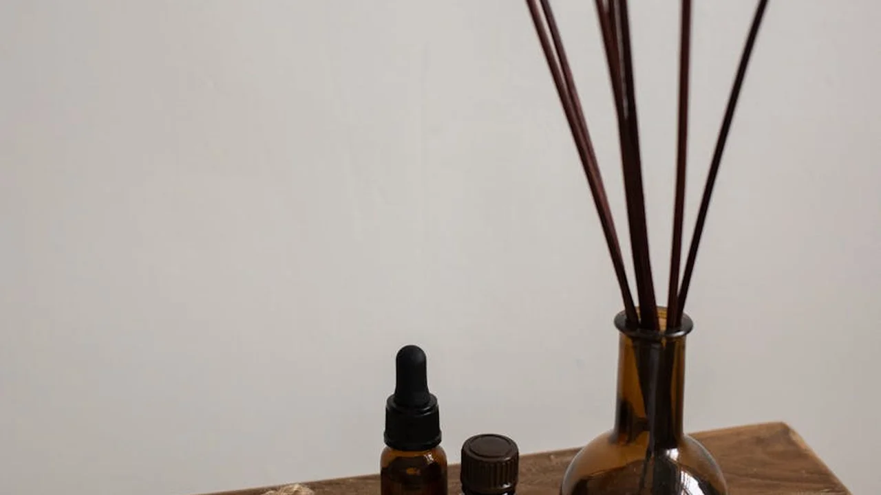 Amber glass dropper bottle with a black cap and a reed diffuser on a light wooden surface.