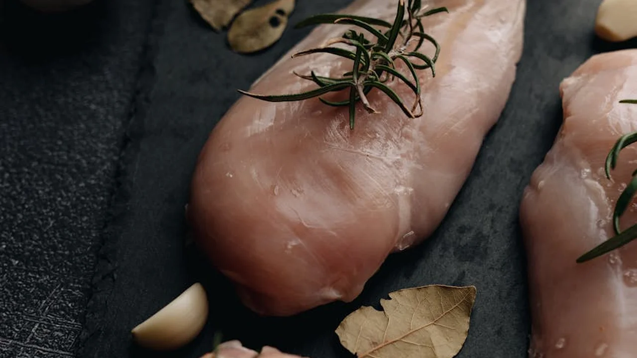 Raw chicken pieces with sprigs of rosemary and garlic on a dark surface