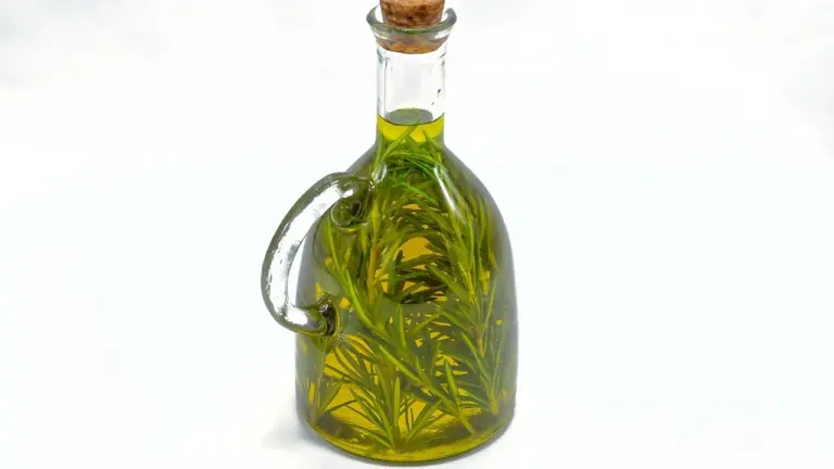 Glass bottle of rosemary-infused oil with fresh rosemary sprigs inside, sealed with a cork stopper, on a white background.