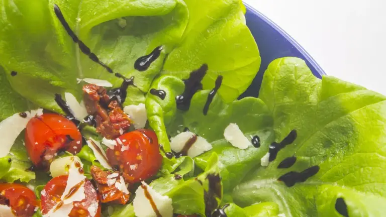 Green lettuce salad with cherry tomatoes, shaved cheese, and a dark balsamic drizzle.