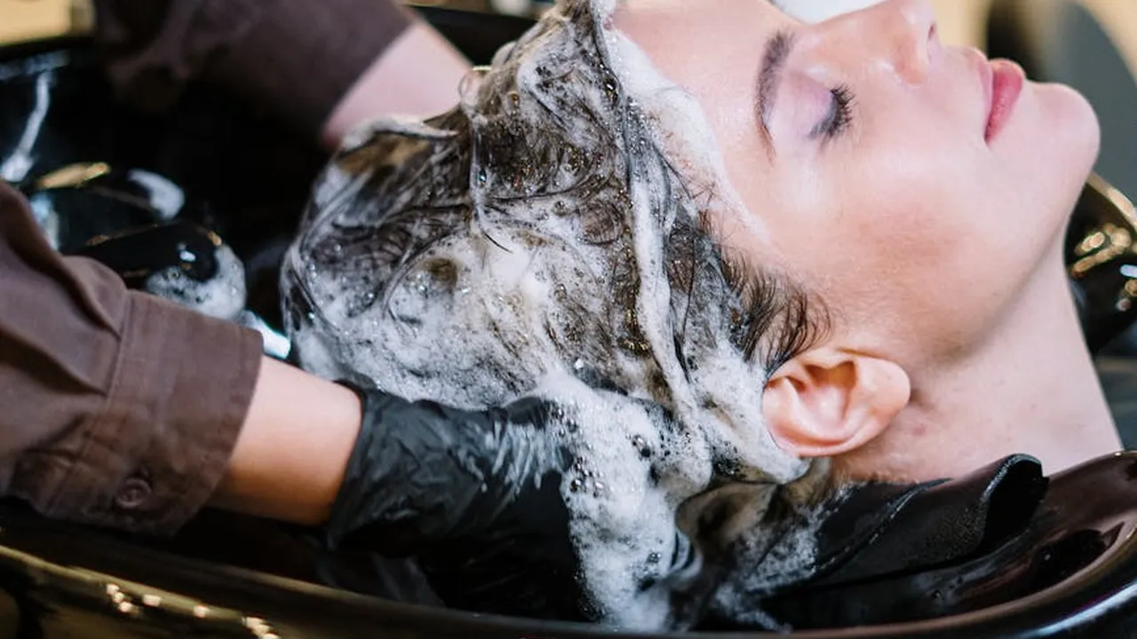 Person in a salon receiving a hair wash with lather in a sink, eyes closed