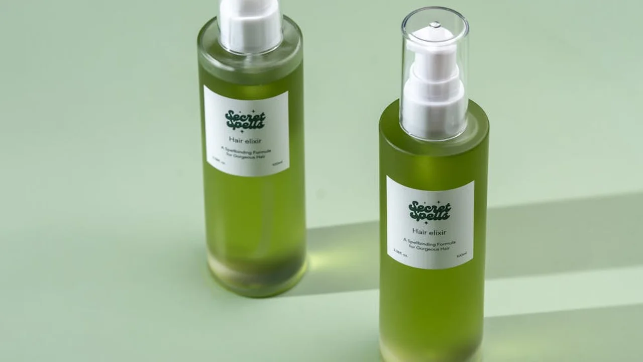 Two green spray bottles with white labels on a pale green surface, containing scalp and hair oil.
