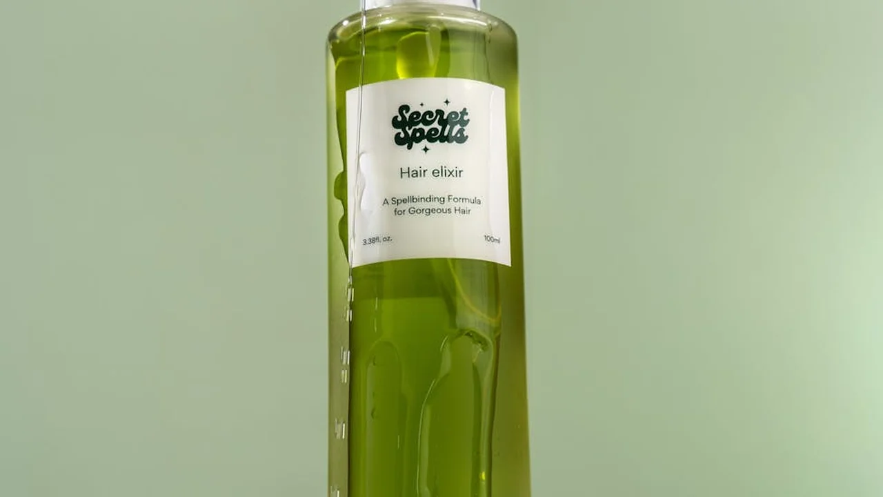 Green glass bottle with a white label reading 'Hair elixir' from Secret Spells against a pale green background