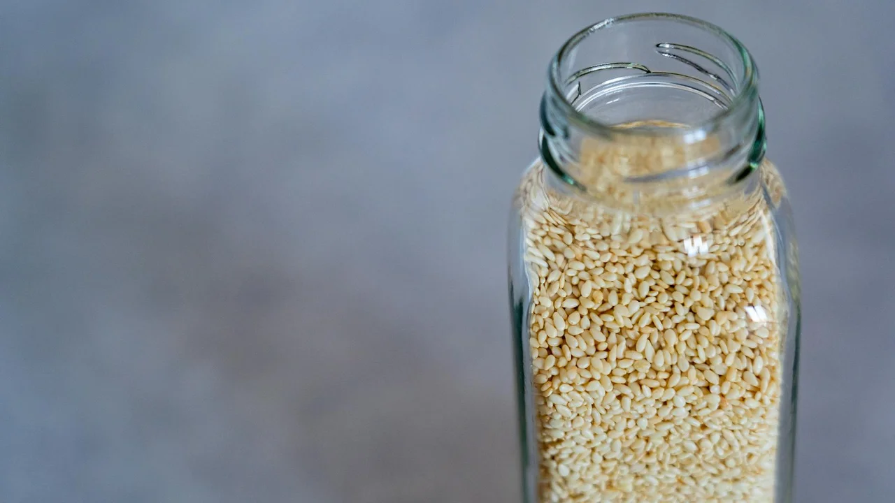 Close-up of a glass bottle filled with pale sesame seeds.