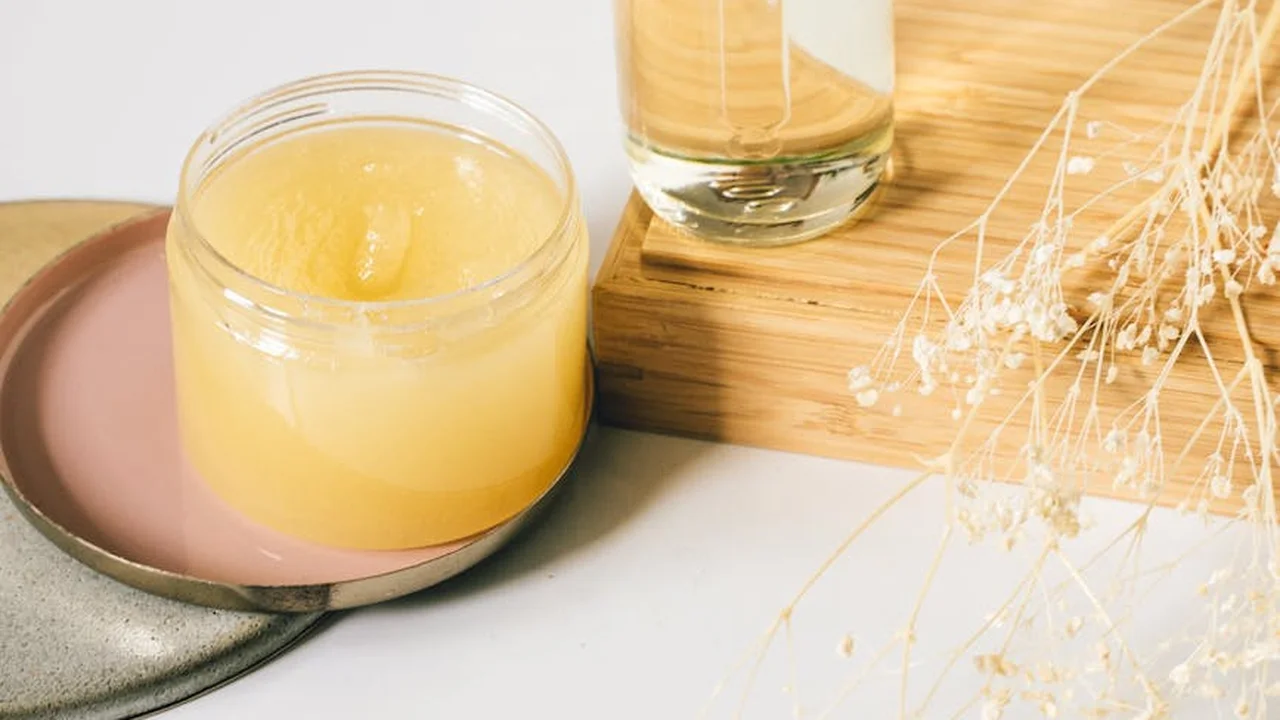A jar of yellow face oil balm on a soft pink surface with two glass bottles of oil and dried botanicals in the background, depicting a simple DIY apothecary setup for skincare.