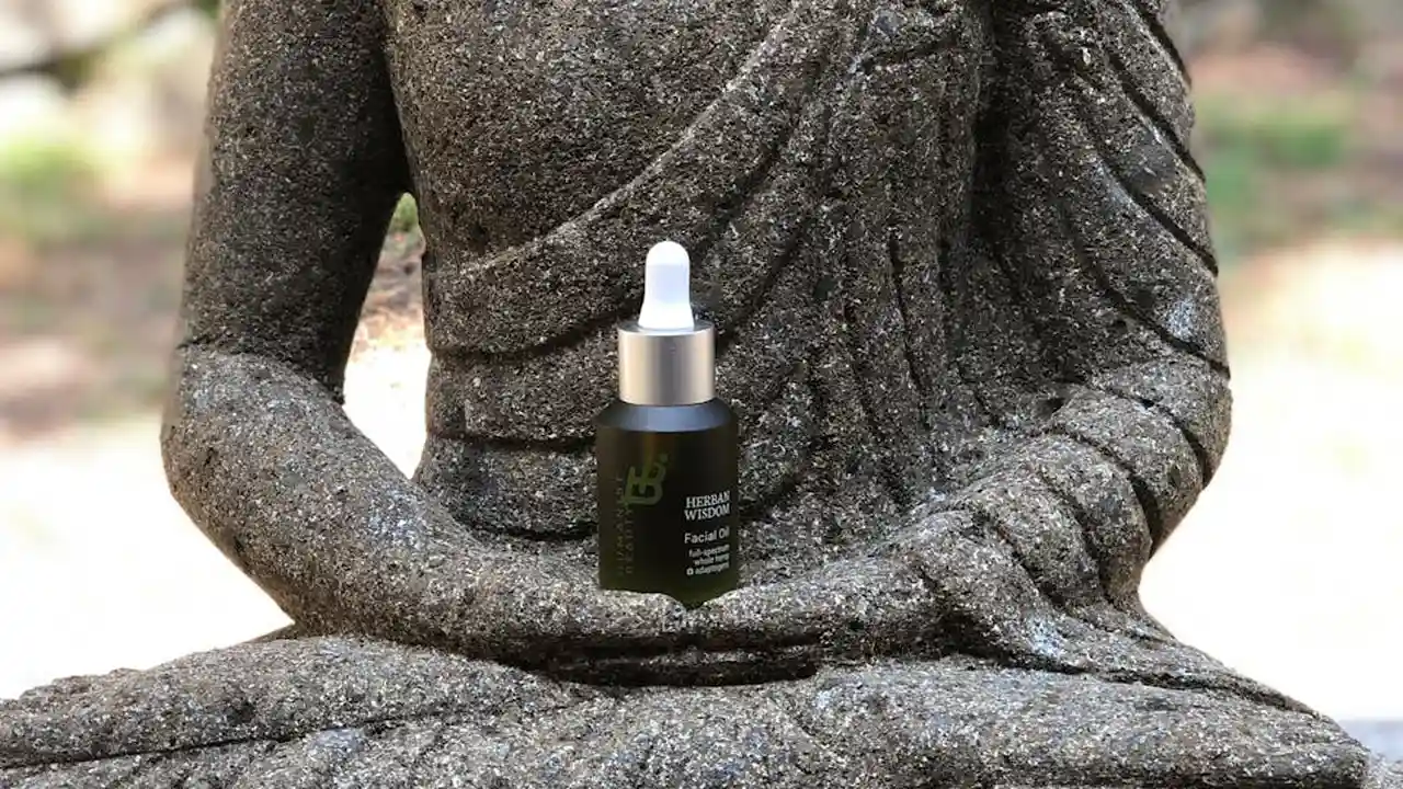 A stone meditative statue with a dropper bottle of facial serum resting on its lap, illustrating skincare layering concepts.