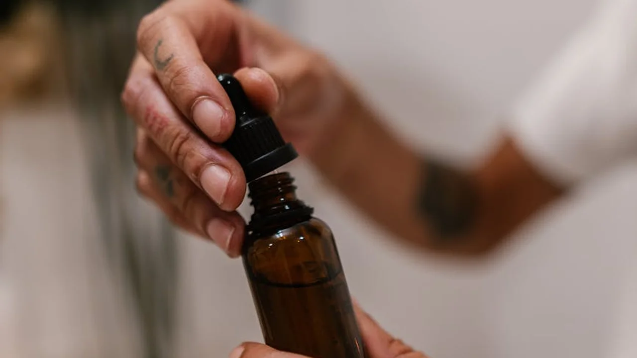 Close-up of a hand holding a dropper bottle, preparing to apply body oil
