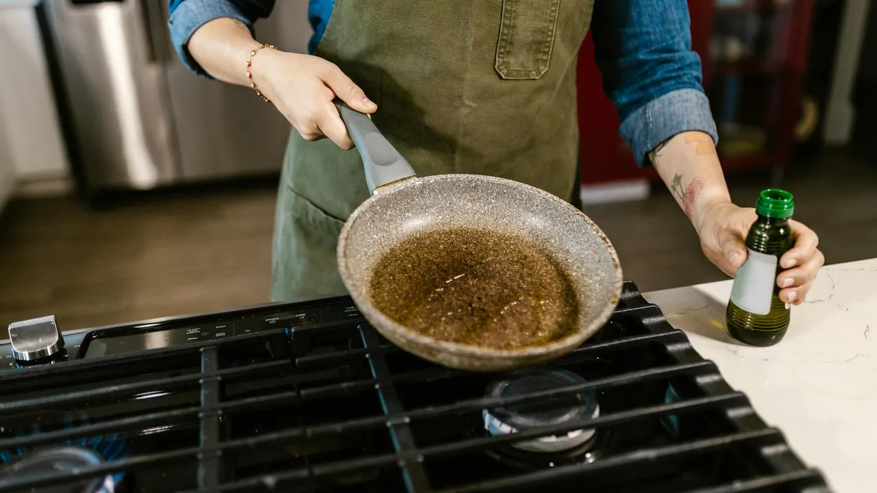 Home cook in an apron holds a pan over a gas stove with browned contents, while reaching for a bottle of oil to illustrate butter-to-oil substitutions.