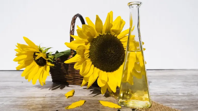 A bottle of cooking oil on a wooden table next to a basket of sunflowers.