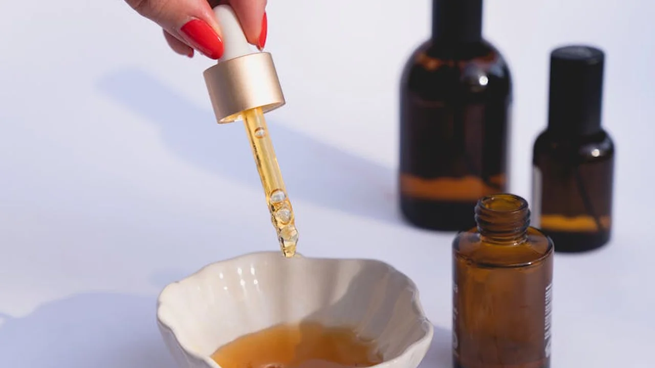 A dropper releases essential oil into a small dish, with amber glass bottles in the background, illustrating how tea tree oil can be found in local stores.