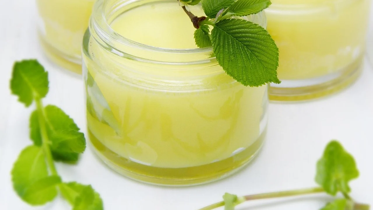 Two small glass jars containing pale yellow oil with fresh mint leaves on a white surface.