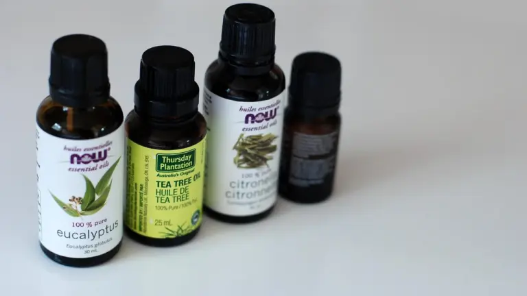 Several essential oil bottles on a white surface, including tea tree oil and citronella, arranged in a row.