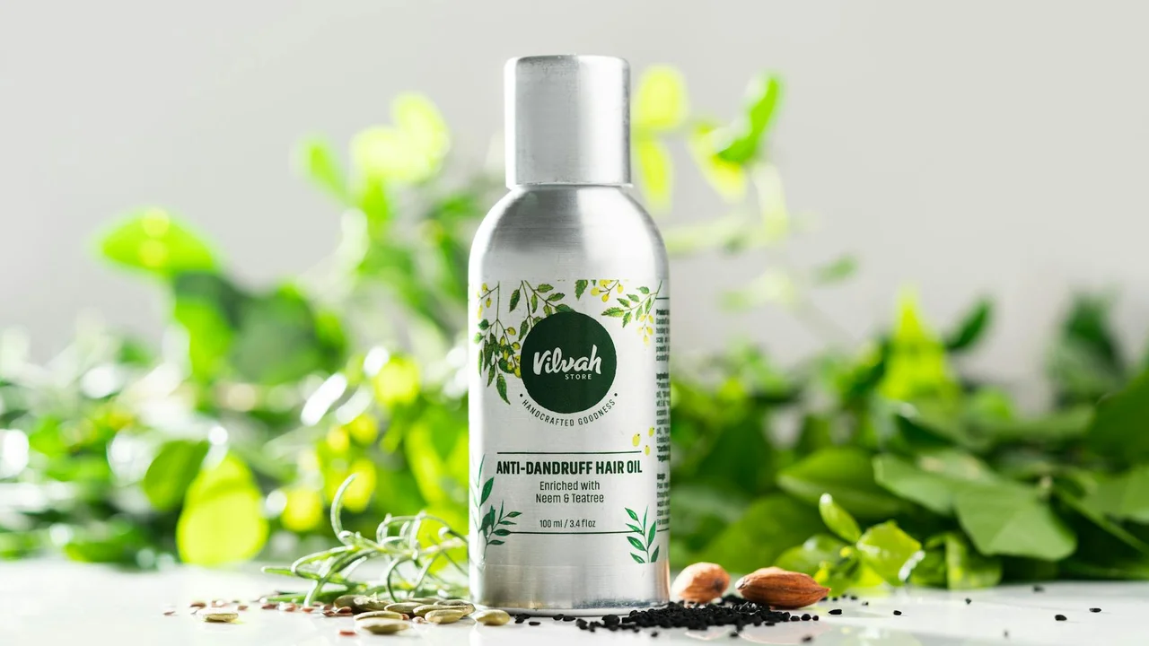 Small bottle of tea tree oil in a bright setting with green leaves in the background.