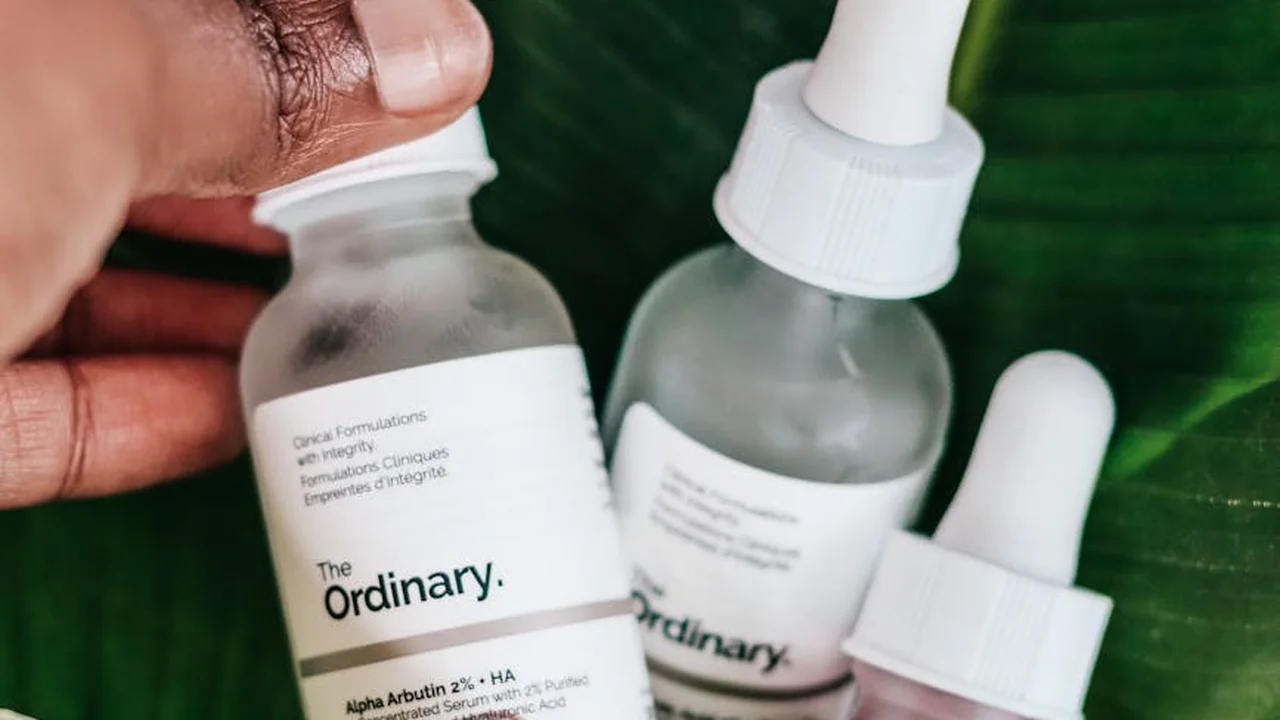 Close-up of The Ordinary skincare bottles with droppers, a hand nearby, green leaves in the background