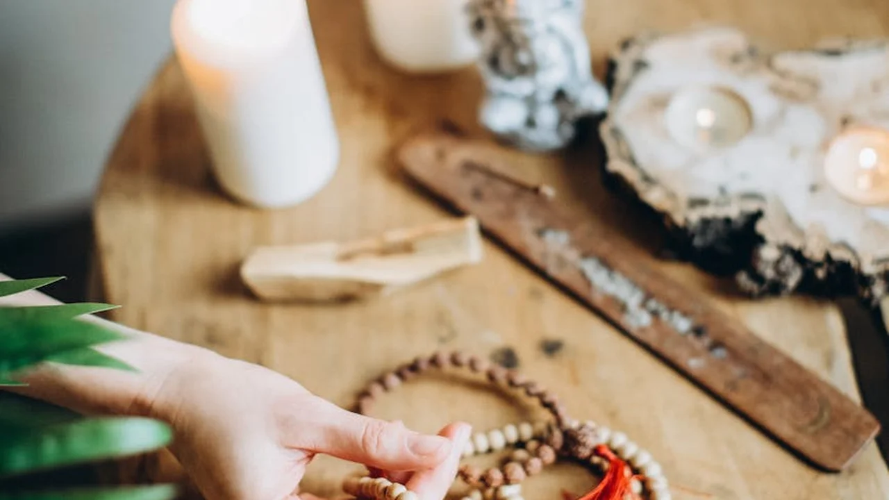 Close-up of a hand resting near a wooden craft table with candles, driftwood, and natural decor, suggesting a cozy workspace for experimenting with fragrance oil measurements in candle making.