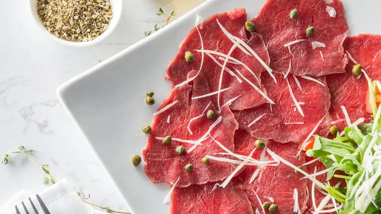 Thinly sliced raw beef arranged on a white plate with shredded onions and green garnish