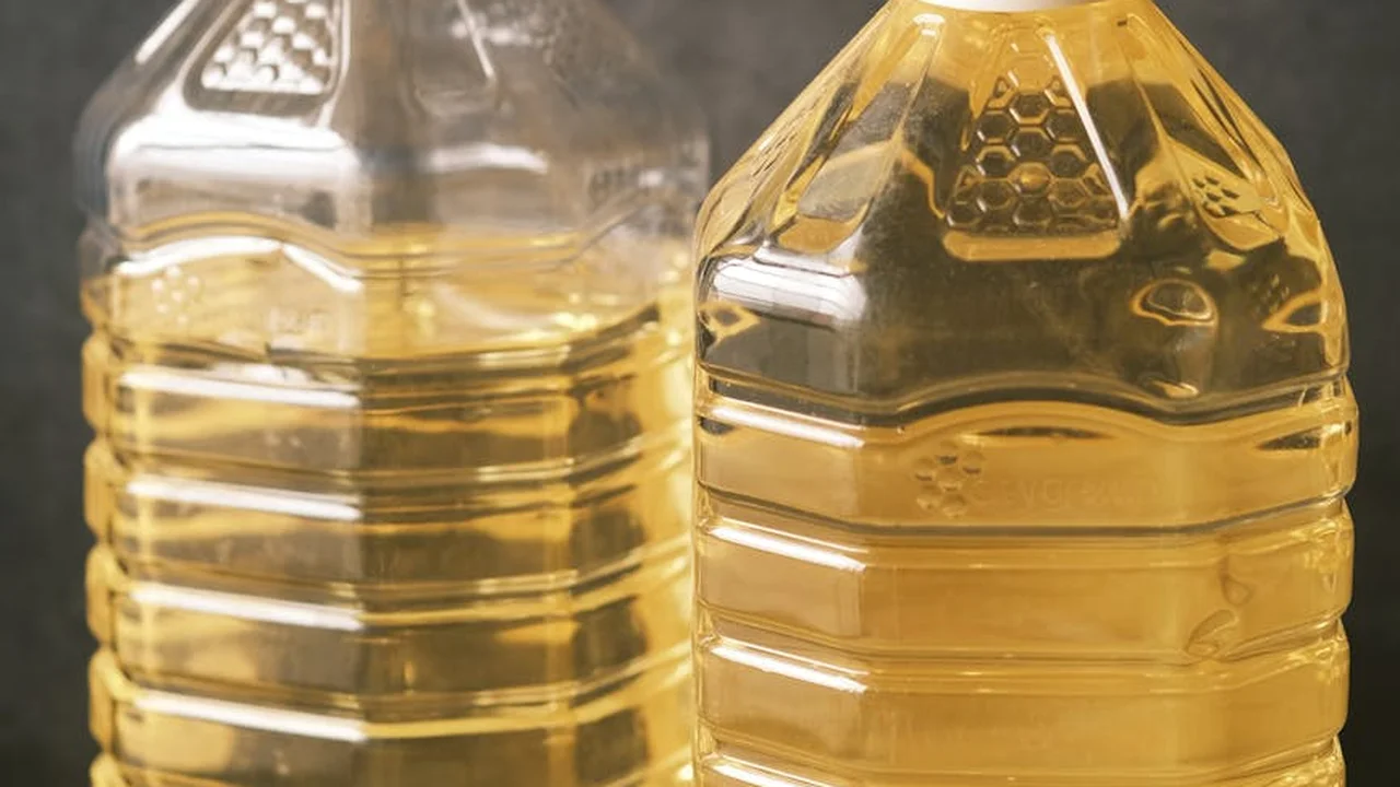 Two clear plastic bottles filled with golden used cooking oil on a kitchen surface.