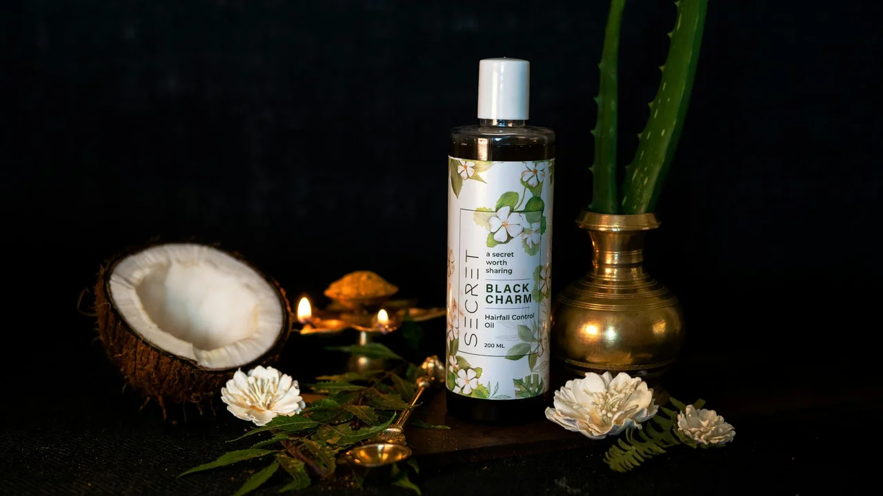 A bottle of hair oil beside a halved coconut, pine cones, and green plants on a dark background.