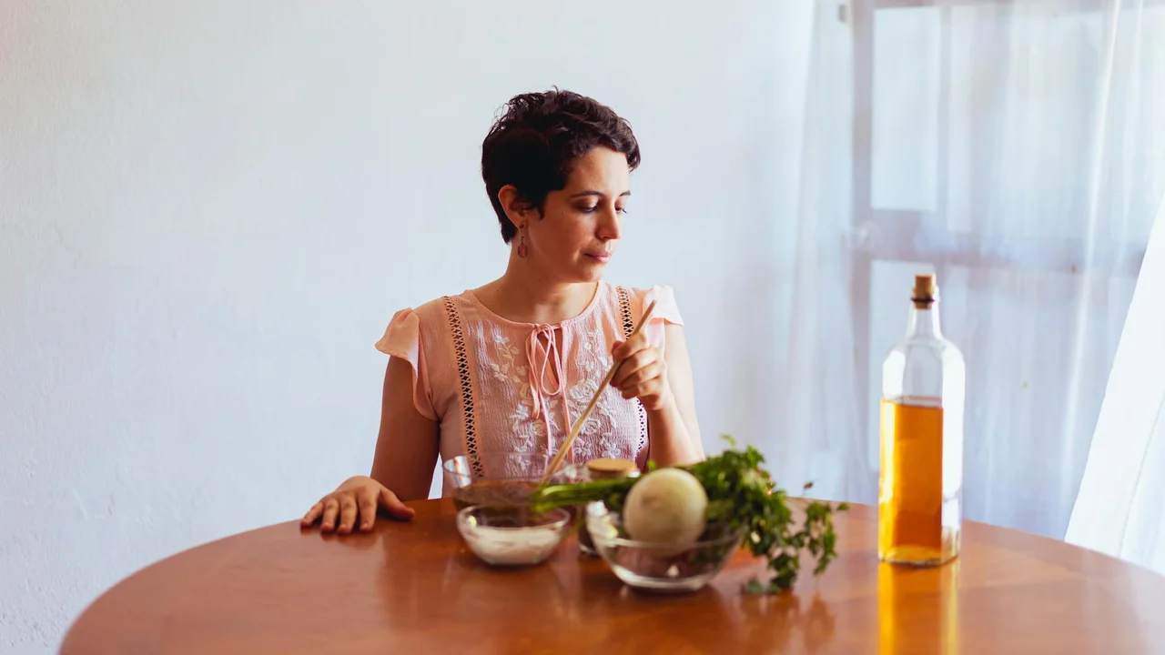 Woman sitting at a kitchen table with a bottle of vegetable oil and fresh vegetables.