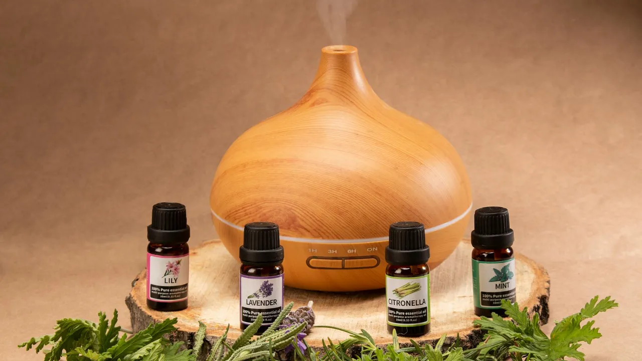 Wooden, dome-shaped essential oil diffuser with a light wood finish, surrounded by small bottles of essential oils on a natural wood surface.
