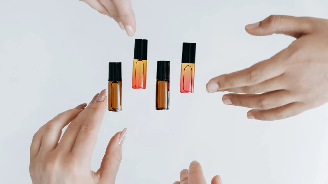 Small amber essential oil bottles floating between hands on a white background.